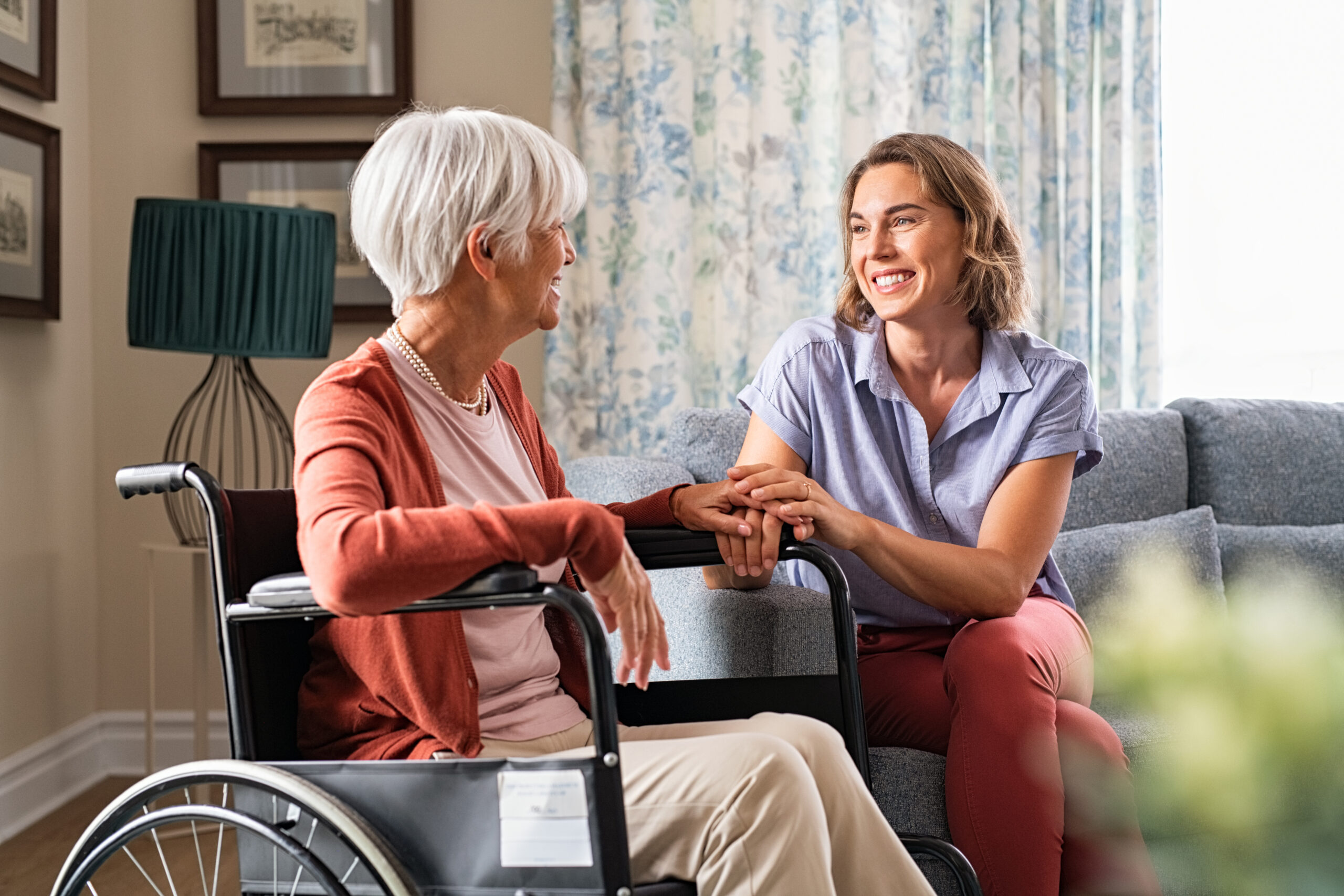 Adult Direct Care Professional comforting senior mom sitting on a wheelchair at home.