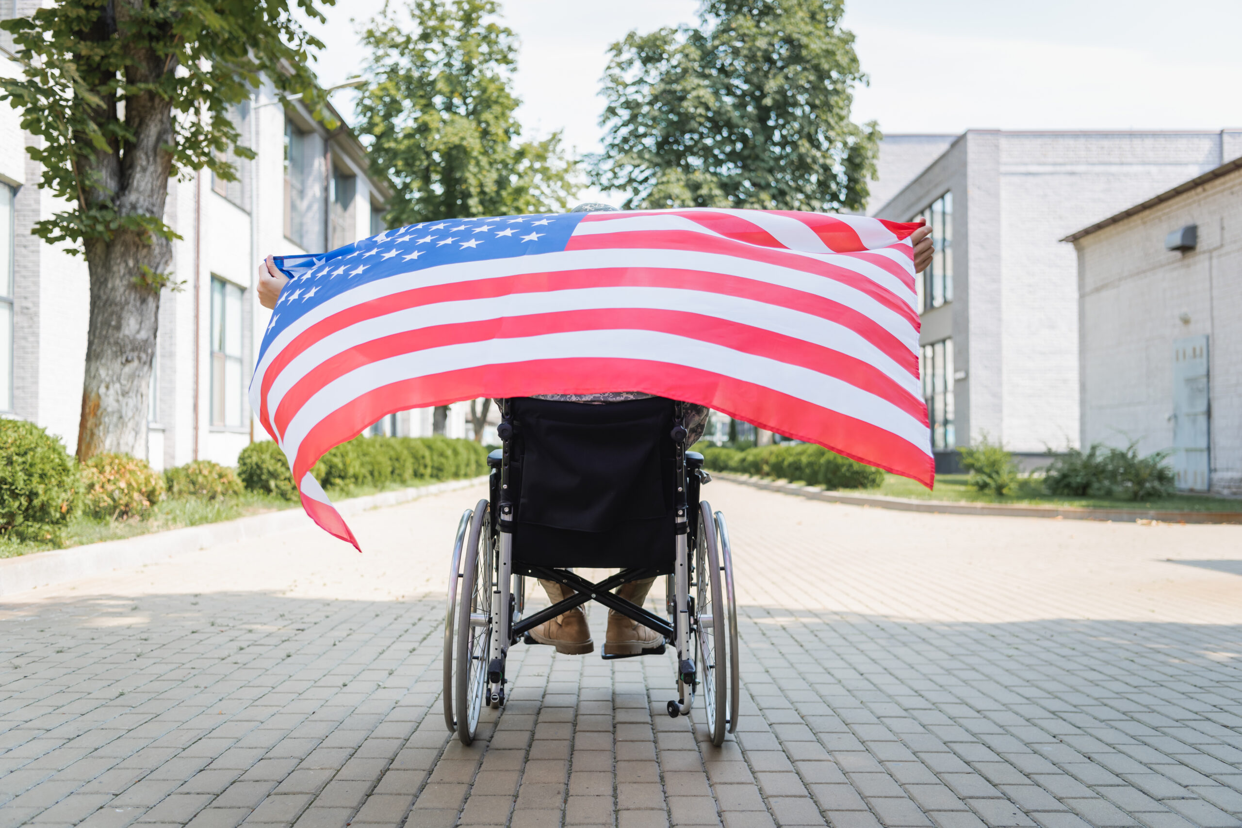 Photo from behind a person in a wheelchair holding an American flag