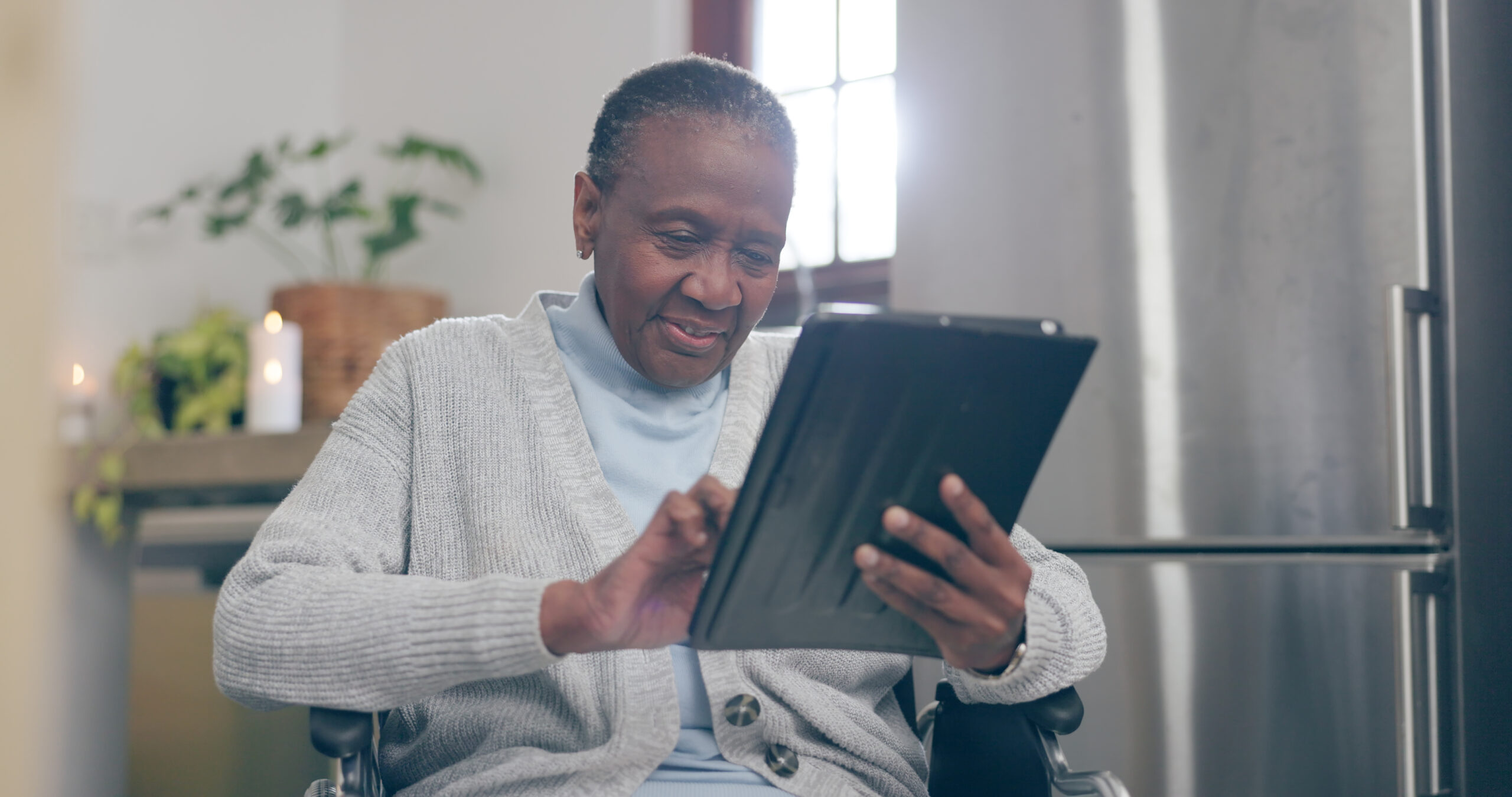 An aging woman, in a wheelchair and using a tablet held in her hands.