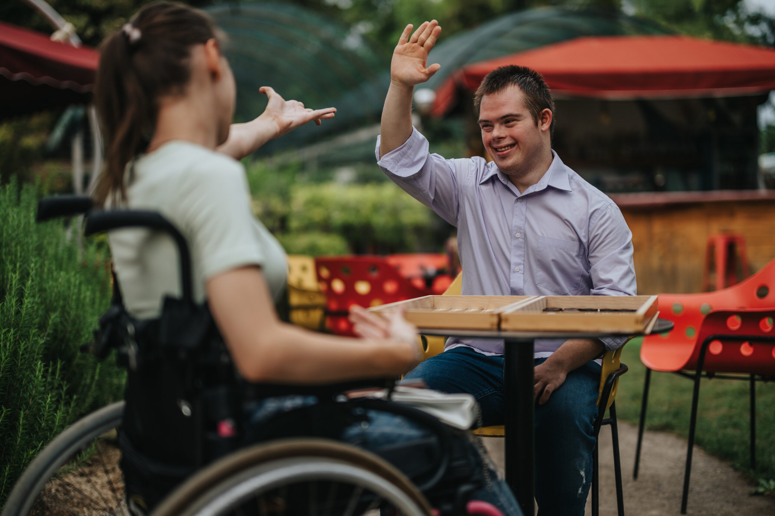 A boy with Down syndrome and a girl in a wheelchair share a conversation at a table.
